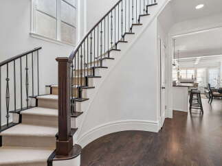 Experience elegant living with this stunning staircase featuring a dark wood banister and intricate metal railings.
