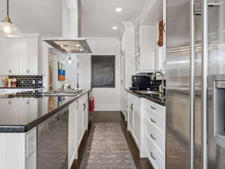 Experience culinary excellence in this stunning modern kitchen, featuring sleek white cabinetry, a spacious granite island with a built-in stovetop, and a professional-grade stainless steel range hood.