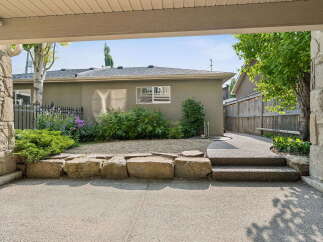 Step into a charming backyard oasis featuring a well-maintained garden with vibrant purple flowers and lush green bushes.