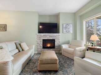 Cozy up by the modern stone fireplace in this inviting living room, featuring plush white leather seating and a large ottoman perfect for relaxation.