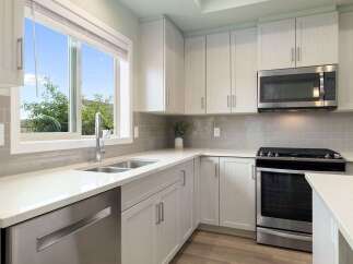 This modern kitchen features sleek white cabinetry and a durable quartz countertop, perfect for meal preparation.