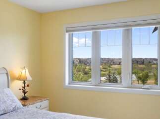 This charming bedroom features a large window offering a picturesque view of a serene pond and a suburban neighborhood.