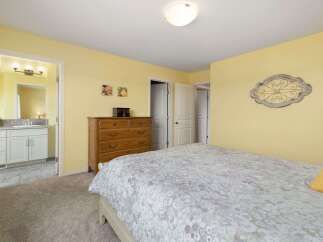 This charming bedroom features a cozy queen-size bed with a light-colored floral comforter, complemented by soft yellow walls.