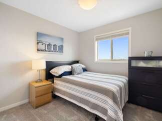 This cozy bedroom features a comfortable bed with a striped comforter, a modern nightstand with a lamp, and a dark dresser with a glass-top drawer.