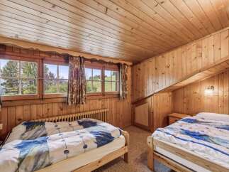Experience rustic charm in this cozy wooden cabin bedroom, featuring two comfortable beds adorned with blue and white patterned duvets.