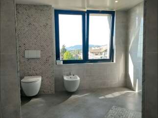 Experience modern luxury in this stunning bathroom featuring a wall-mounted toilet and bidet, complemented by elegant mosaic tile accents.