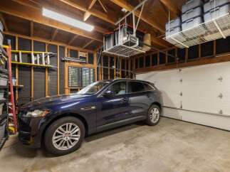 This spacious garage offers ample storage solutions with overhead shelving and a tall shelving unit, perfect for organizing tools and seasonal items.