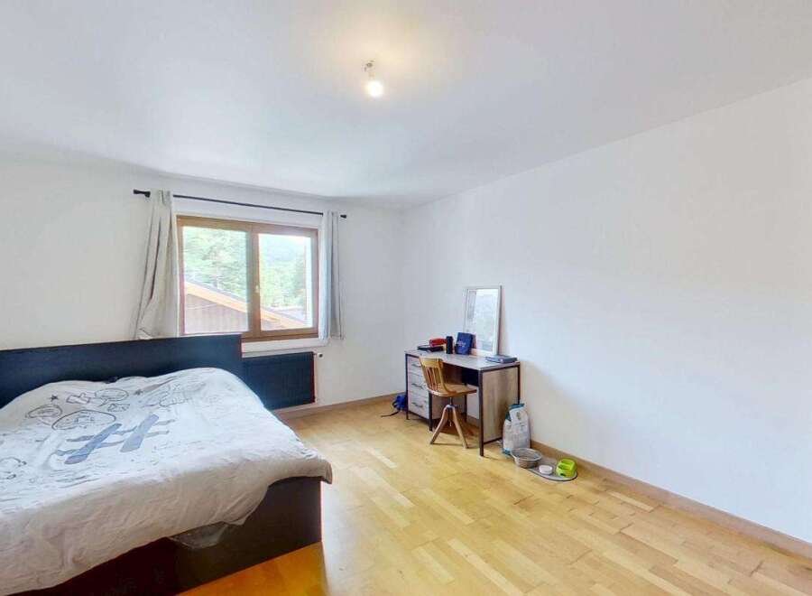 Discover this cozy bedroom featuring a comfortable bed with a unique duvet cover, a functional desk area with a wooden chair, and a large window offering scenic views.