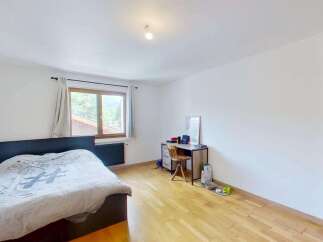 Discover this cozy bedroom featuring a comfortable bed with a unique duvet cover, a functional desk area with a wooden chair, and a large window offering scenic views.
