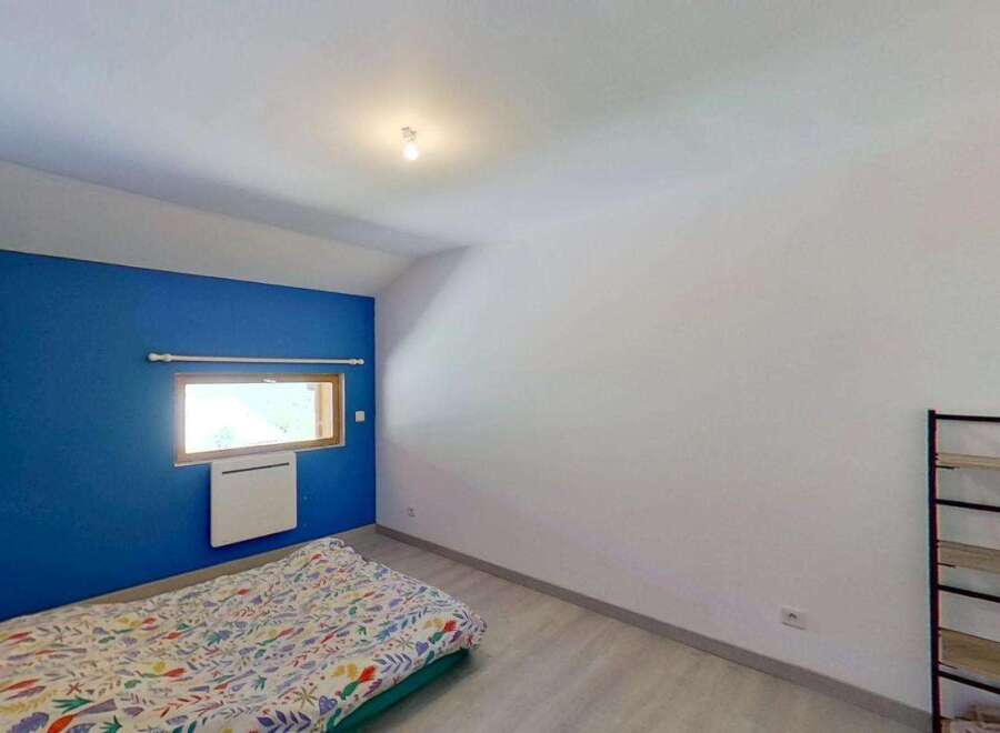 Discover this charming bedroom featuring a vibrant blue accent wall and a comfortable bed with a colorful duvet.