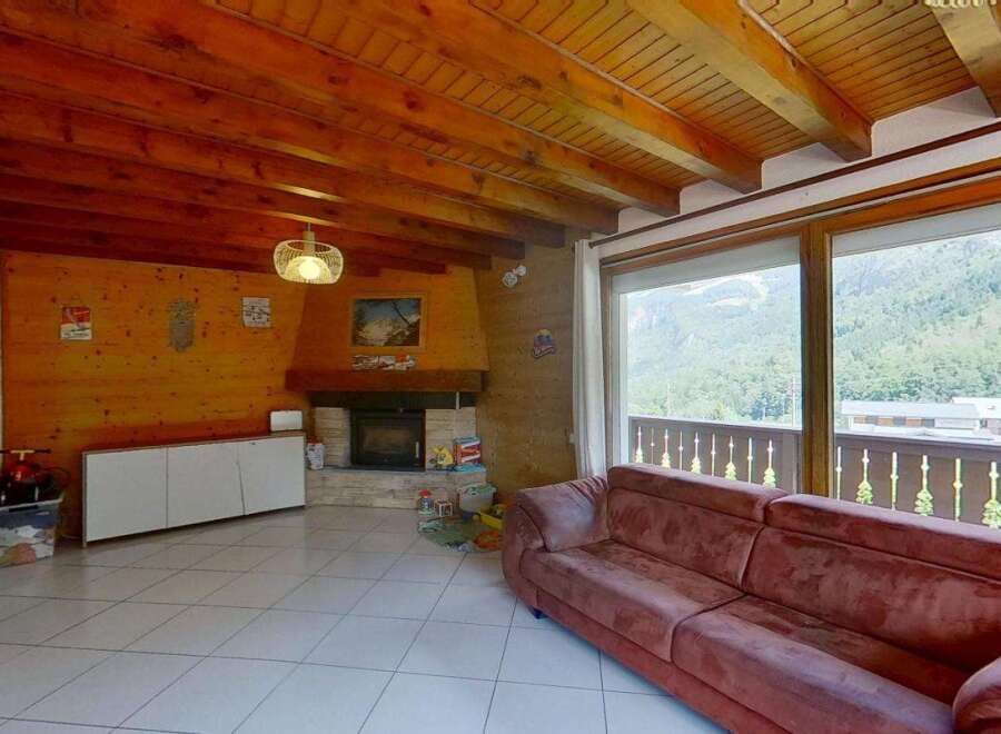 Experience cozy mountain living in this charming living room featuring a rustic stone fireplace and warm wood-paneled walls.