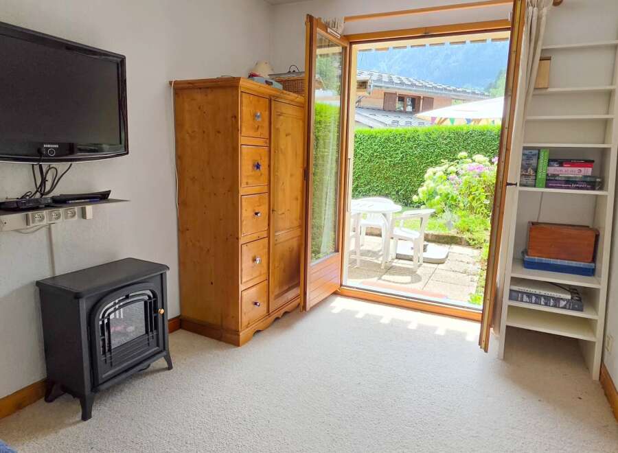 This cozy living space features a modern Samsung TV mounted on the wall, complemented by a charming wooden armoire and a compact electric fireplace for warmth.
