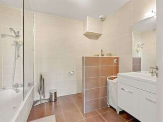 This modern bathroom features a sleek bathtub with a glass shower screen, complemented by warm-toned tiled walls and floors.