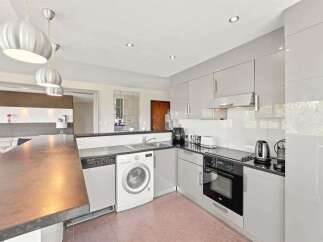 This modern kitchen features sleek, high-gloss cabinetry and a spacious breakfast bar, perfect for casual dining.