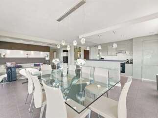 Experience modern luxury in this open-concept living and dining area, featuring a sleek glass dining table with contemporary chairs.