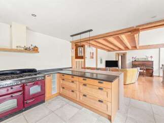 Experience rustic charm in this open-plan kitchen and living area, featuring a striking red range cooker and a spacious wooden island perfect for meal preparation.