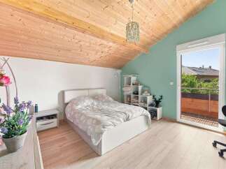 This charming attic bedroom features a cozy bed with a patterned duvet, complemented by a light wood-paneled ceiling and light wood flooring.
