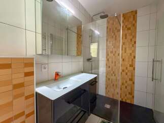 Discover this modern bathroom featuring a sleek vanity with an orange faucet, complemented by a spacious shower enclosure with decorative tiled accents.