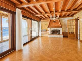 Experience breathtaking lake views from this stunning living room, featuring a grand fireplace and a beautiful wood-beamed ceiling.