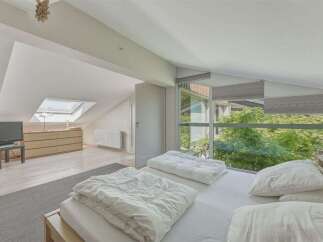 Experience modern living in this attic bedroom featuring a skylight and large windows offering lush green views.