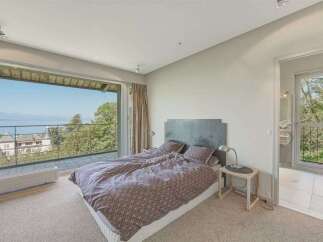 Experience breathtaking lake and mountain views from this stunning bedroom, featuring a spacious king-sized bed with a patterned duvet and a modern headboard.