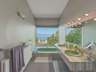 Experience luxury in this stunning bathroom featuring a vibrant green bathtub with a breathtaking view of a lake and distant mountains.