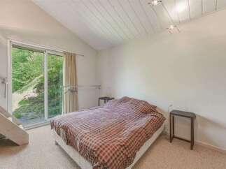 This charming bedroom features a vaulted ceiling with exposed beams and a large sliding glass door that opens to a lush green outdoor space.
