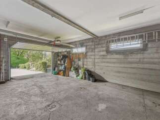 Discover this spacious garage featuring a large overhead door opening to a lush green exterior.