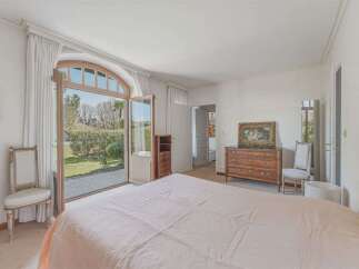 Experience luxurious living in this spacious bedroom featuring a grand arched doorway that opens to a lush garden view.