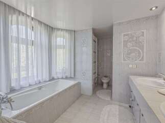 Experience luxury and relaxation in this elegant bathroom featuring a deep soaking tub bathed in natural light from large, sheer-draped windows.