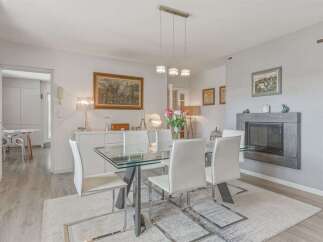 This elegant dining room features a modern glass-top dining table with sleek white chairs, perfect for hosting guests.