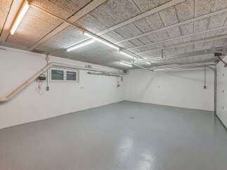 Discover this spacious garage featuring a clean, grey concrete floor and bright fluorescent lighting, perfect for vehicle storage or a workshop.