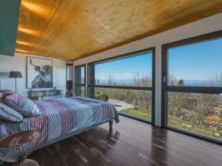 Experience breathtaking panoramic views from this stunning bedroom, featuring expansive windows that showcase the natural landscape.