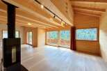 Experience modern mountain living in this stunning wooden interior featuring a sleek black wood-burning stove and expansive windows that frame breathtaking forest views.