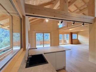 Experience modern mountain living in this stunning wooden chalet, featuring an open-concept living space with panoramic windows showcasing breathtaking forest views.