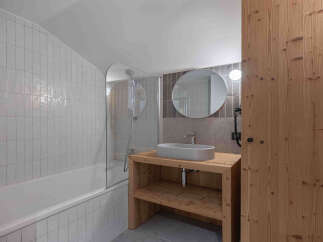 This modern bathroom features a sleek bathtub with a glass shower screen, complemented by vertical white tilework.