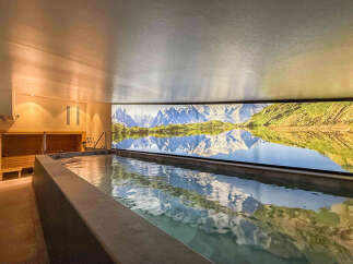 Experience ultimate relaxation in this luxurious spa featuring a serene indoor pool with a stunning mountain and lake mural.