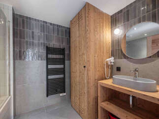 Experience modern comfort in this stylish bathroom, featuring a sleek grey tiled shower area and a rustic wooden vanity.