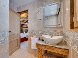 This charming bathroom features a modern vessel sink atop a rustic wooden vanity, complemented by elegant stone tilework.