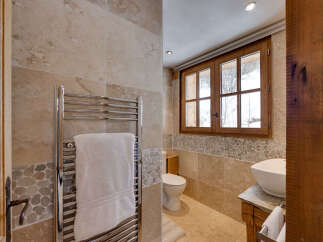 This luxurious bathroom features a modern chrome towel warmer with a plush white towel, complementing the natural stone tile walls.