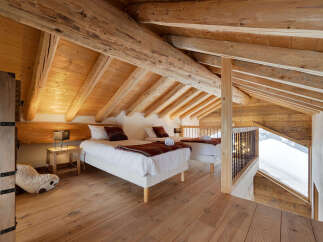 Experience rustic charm in this attic bedroom featuring two cozy beds with warm-toned blankets and pillows.