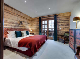 Experience rustic charm in this cozy bedroom, featuring a luxurious king-size bed adorned with plush pillows and a warm red throw.