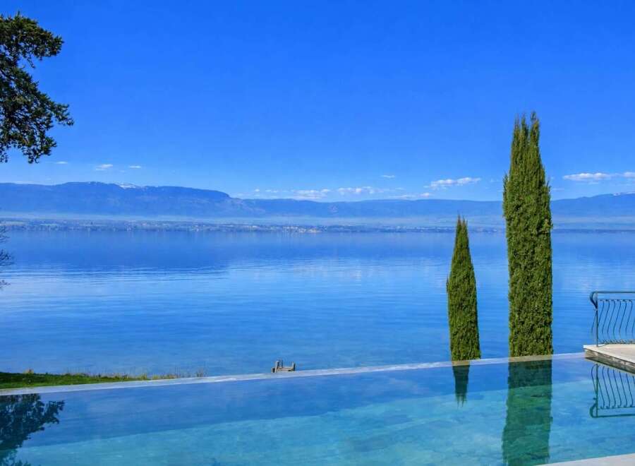 Experience luxury living with this stunning infinity pool overlooking a serene lake and majestic mountains.