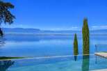 Experience luxury living with this stunning infinity pool overlooking a serene lake and majestic mountains.