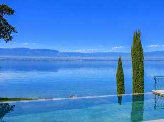 Experience luxury living with this stunning infinity pool overlooking a serene lake and majestic mountains.