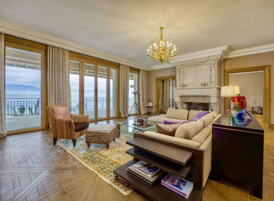 Experience luxurious living in this elegant living room, featuring a grand fireplace and expansive glass doors that open to breathtaking water views.