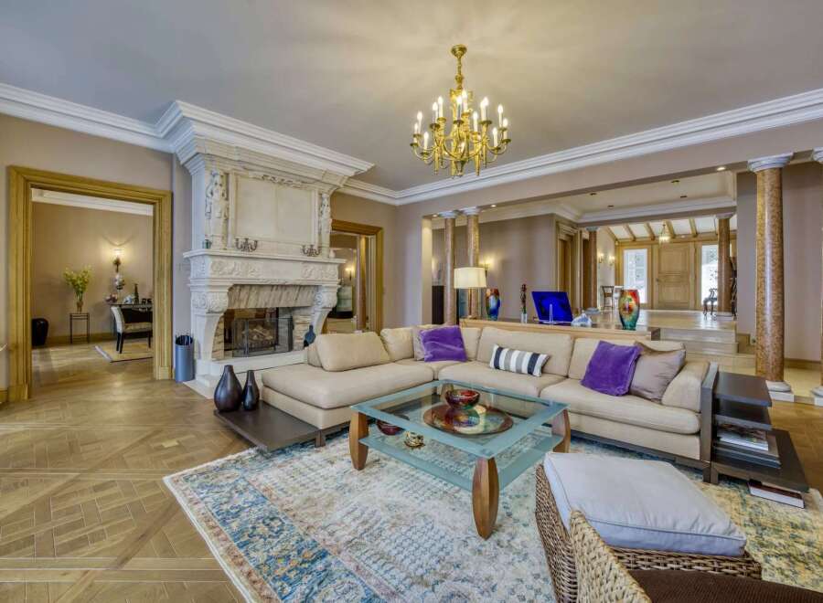 Experience opulent living in this grand living room, featuring a magnificent ornate fireplace and a luxurious sectional sofa adorned with plush accent pillows.
