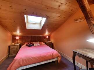 This charming attic bedroom features a cozy ambiance with its warm wooden ceiling and walls, complemented by a bright skylight.