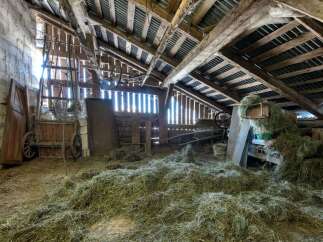 Discover the rustic charm of this barn, featuring a traditional wooden cart and ample hay storage, perfect for agricultural use or conversion.
