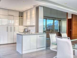 Experience modern luxury in this stunning kitchen featuring sleek, high-gloss white cabinetry and a convenient island with a built-in sink.